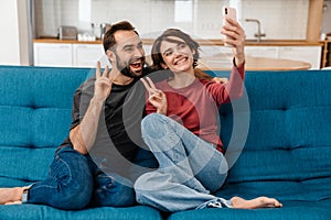 Happy young couple showing peace sign while taking selfie on cellphone