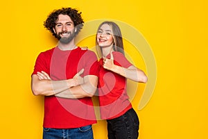 Happy young couple showing thumbs up and looking at the camera over yellow backgroun