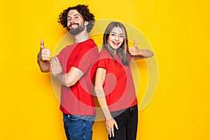 Happy young couple showing thumbs up and looking at the camera over yellow backgroun