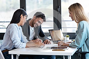 Happy young couple signing bank loan agreement with real-estate agent to buying the house in the office