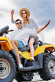 happy young couple sitting on ATV in front of cloudy sky and looking