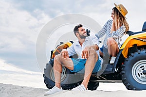 happy young couple sitting on ATV on sandy dune in front of