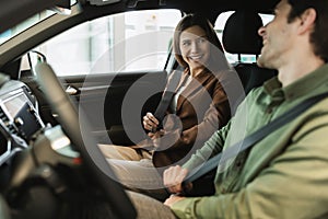 Happy young couple sitting in automobile salon, satisfied with test drive, discussing purchase of new car at auto