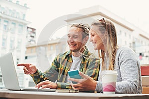 Happy young couple sitting in cafe with laptop and discussing plans together