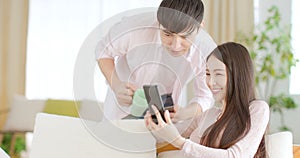 Happy young couple sitting on  couch and  looking at mobile phone