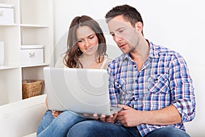 Happy young couple sitting on couch using laptop