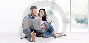 Happy young couple sitting on the floor with a laptop looking for their new home and furniture. Mock up
