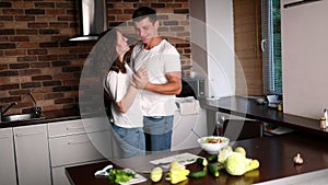 Happy young couple smiling and dancing in the kitchen while preparing dinner. Loving man and woman having fun at home.