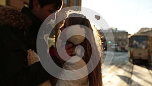 Happy young couple softly kissing on sunset in winter. City life and traffic jam on background