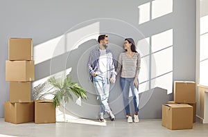 Happy young couple standing against the wall with cardboard boxes in a new apartment on moving day.