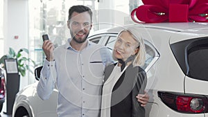 Happy young couple standing near their new car at the dealership