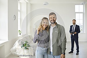 Happy young couple standing in their new house, smiling and showing the key to new home