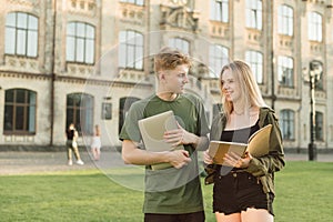 Happy young couple of students are outdoors on campus at the University, holding a laptop and a notebook in their hands, smiling