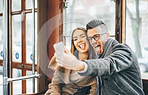 Happy young couple taking photos using mobile smart phone camera inside bus - Travel lovers making a self portrait