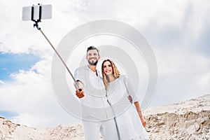 happy young couple taking selfie with monopod and smartphone