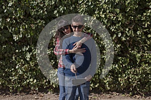 happy young couple taking a selfie with smartphone on the stick over green ivy background. The man is holding the stick and