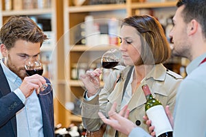 happy young couple tasting wine with merchant in foreground
