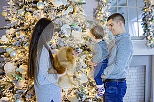 Happy young couple and their baby son near Christmas tree at home