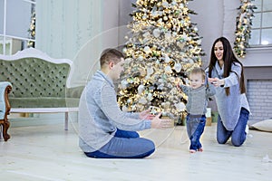 Happy young couple and their baby son near Christmas tree at home