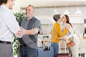 Happy young couple together with luggage coming to parents. Elderly man and woman joyfully welcoming children in hallway