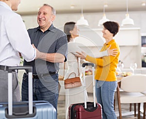 Happy young couple together with luggage coming to parents. Elderly man and woman joyfully welcoming children in hallway