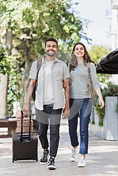Happy young couple travelers walking around the city with luggage. Two beautiful smiling lovers traveling europe.