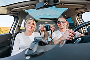 A happy young couple with two daughters inside the car during auto trop. They are smiling, and laughing during a road trip. Family photo