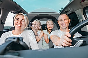 Happy young couple with two daughters inside car during auto trop. They are smiling, laughing during road trip. Family values,