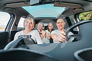 Happy young couple with two daughters inside car during auto trop. They are smiling, laughing during road trip. Family values, photo