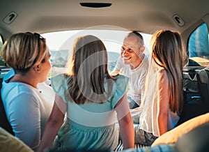 Happy young couple with two daughters inside the car trunk during auto trop. They are smiling, laughing and chatting. Portrait of photo