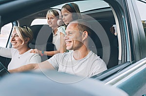 Happy young couple with two daughters inside the modern car with panoramic roof during auto trop. They are smiling, laughing photo