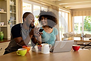 Happy young couple using computer and mobile phone in the kitchen