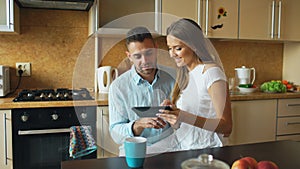 Happy young couple using digital tablet computer while sitting in the kitchen and having breakfast in the morning
