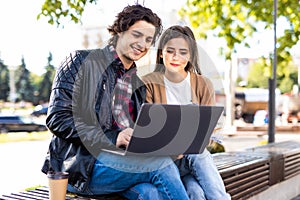 Happy young couple using laptop computer sitting on bench in city outdoor
