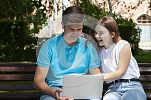 Happy young couple using laptop computer sitting on bench in city outdoor - Concept of relationship and people addicted to