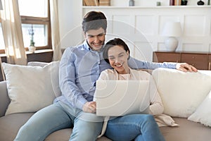 Happy young couple using laptop, relaxing on couch together