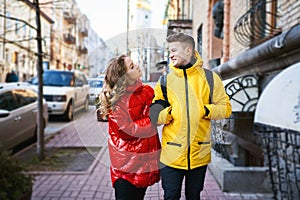 Happy young couple walking city street, looking at each other with smile, wearning in bright yellow and red down jackets