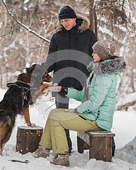 Happy young couple walking with dog in winter forest