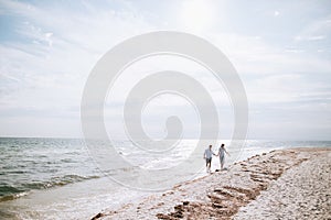 Happy young couple walking on the sea beach holding hands. Summer vacation