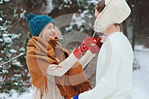 Happy young couple walking in winter snowy forest in warm knitted gloves