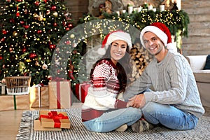 Happy young couple wearing Santa hats in room decorated for Christmas