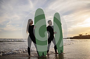 Happy Young Couple In Wetsuits Surfing On The Beach Together