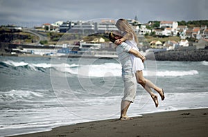Happy young couple on windy beach with black volcanic sand in honneymoon. Man holding beautiful girl on hands photo