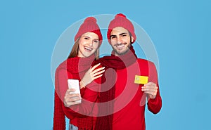 Happy Young Couple In Winter Hats Holding Smartphone And Credit Card