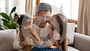 Happy young dad cuddle relax with little daughters at home