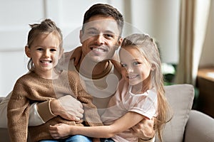 Happy young dad embracing cute kids daughters looking at camera