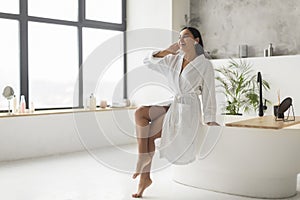 Happy young eastern lady in bathrobe listening to music