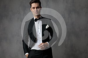 Happy young elegant man wearing tuxedo on grey background