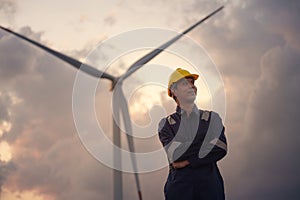 Happy young engineer in uniform with standing in wind turbine farm field