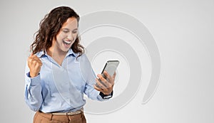 Happy young european woman with open mouth look at phone, celebrate success, win with fist raised up